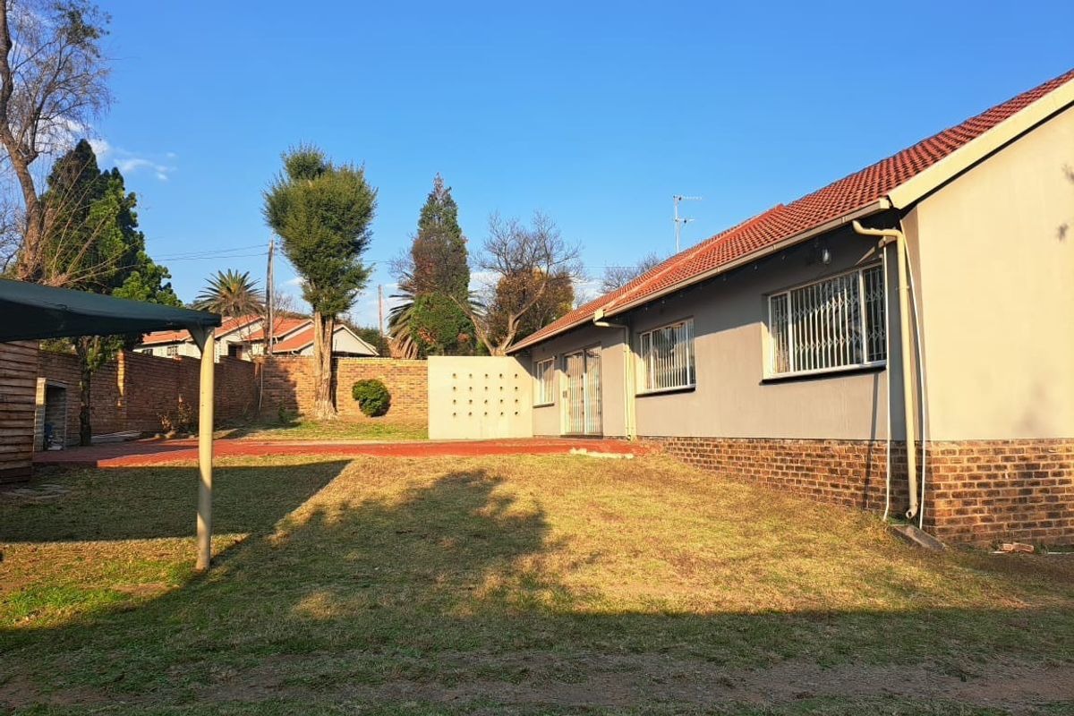 Rear view of the property featuring a paved patio area, brick boundary wall, and a spacious garden with established trees.