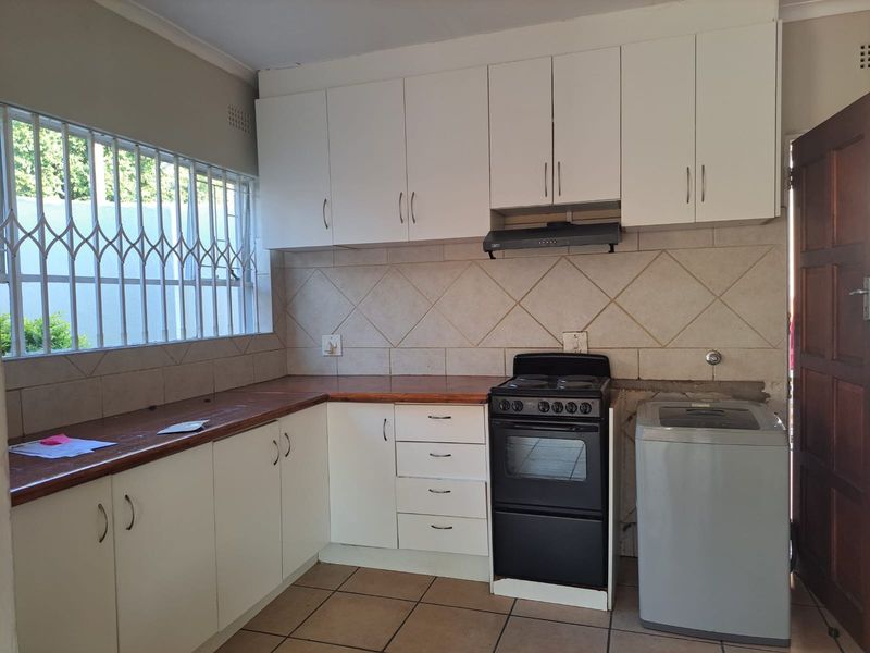 Functional kitchen featuring white cabinetry, tiled backsplash, wooden countertops, and built-in extractor fan, with space for a freestanding stove and washing machine.