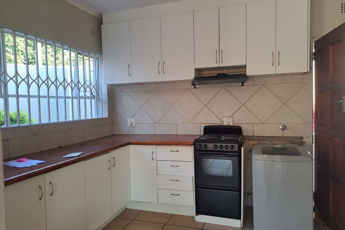 Functional kitchen featuring white cabinetry, tiled backsplash, wooden countertops, and built-in extractor fan, with space for a freestanding stove and washing machine.