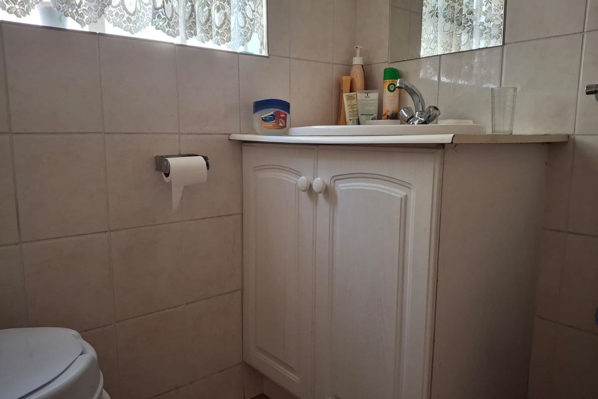 A functional bathroom featuring a vanity cabinet with a basin, wall-mounted mirror, and tiled walls.