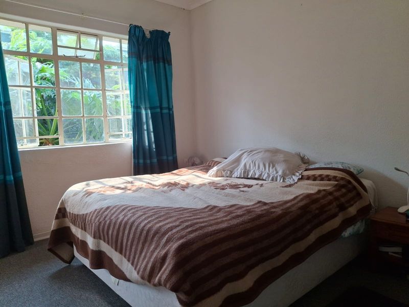 A functional bedroom featuring a large multi-pane window that allows for natural light and garden views.