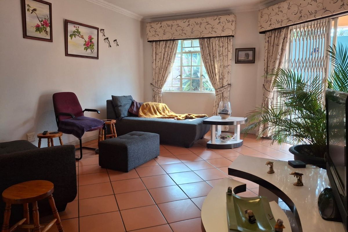 A living room featuring terracotta floor tiles, a sliding glass door with security gate, and decorative cornice detailing.