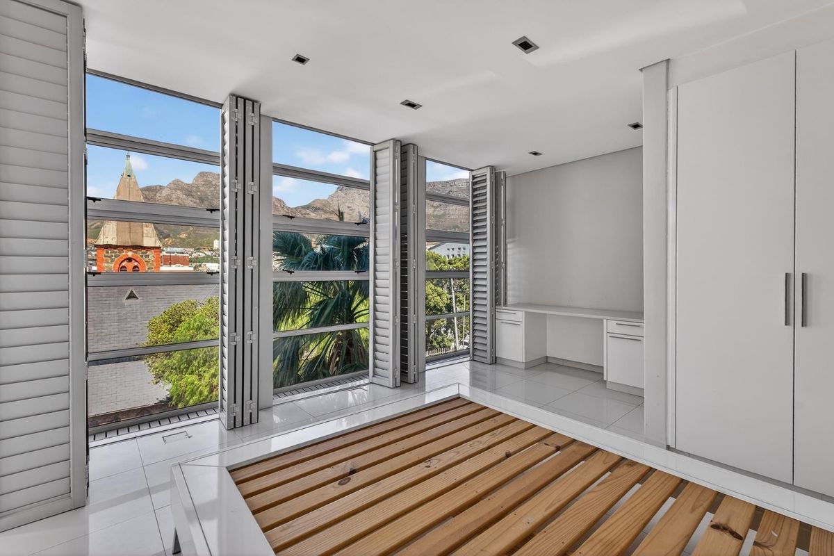 A bright bedroom featuring floor-to-ceiling windows with mountain views, built-in cabinetry, a desk area, and sleek tiled flooring.