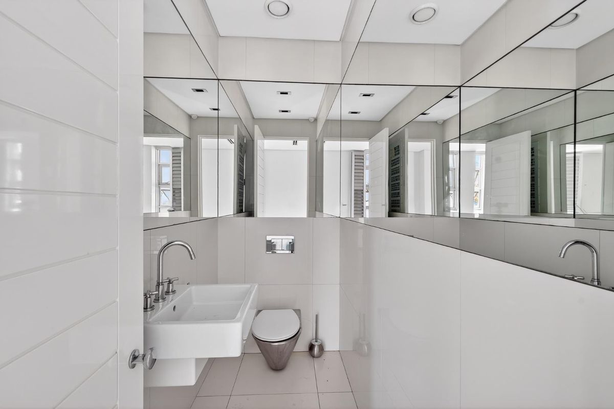 Modern guest bathroom featuring a wall-mounted basin, concealed cistern toilet, and extensive wall-to-wall mirror paneling for a bright, spacious feel.