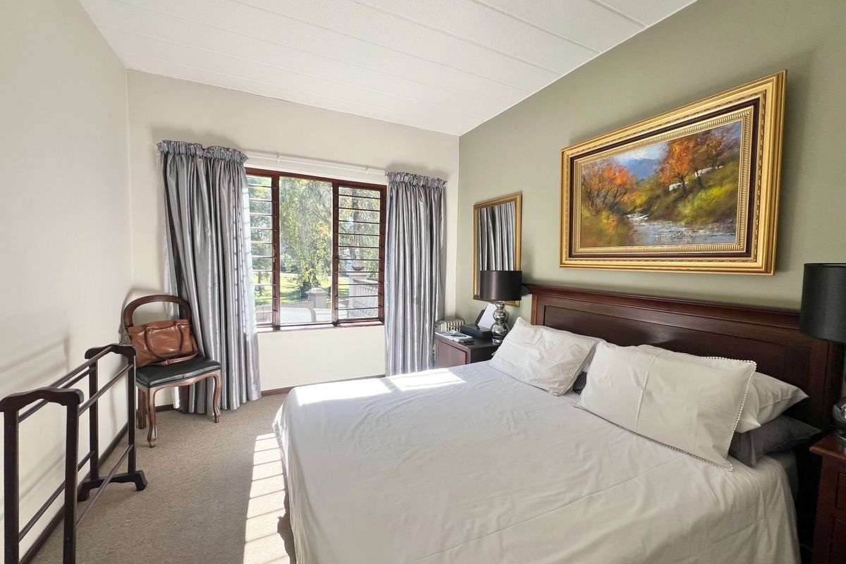 A well-lit bedroom featuring carpeted flooring, a large window with horizontal security bars, and a neutral color palette.