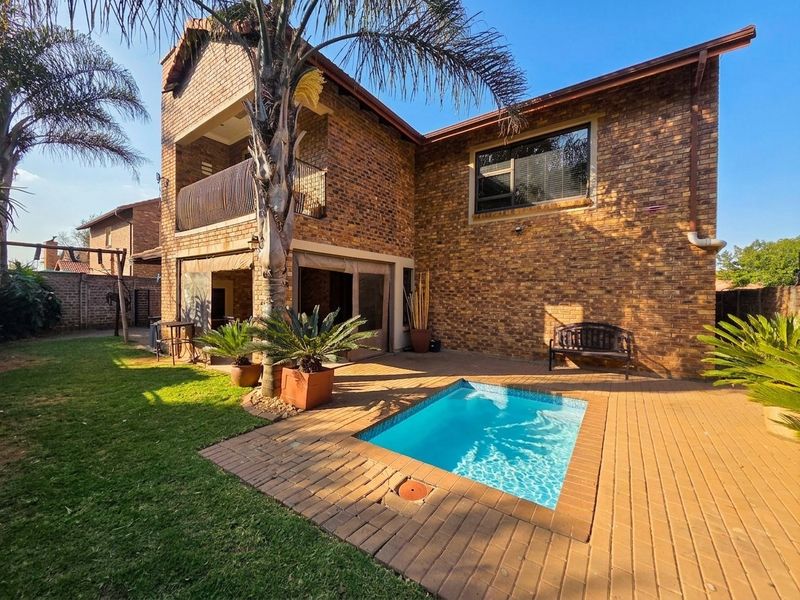 Rear view of a double-story brick house featuring a paved patio area, a small swimming pool, and a balcony overlooking the garden.