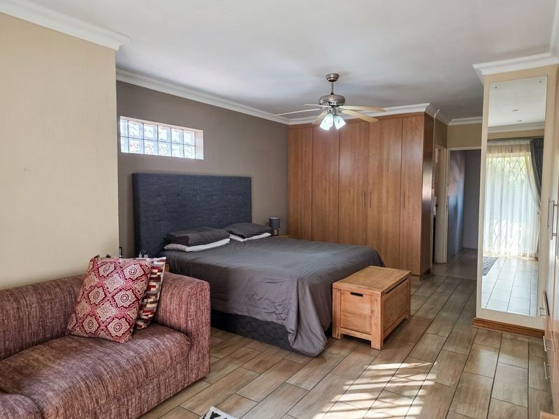 Spacious bedroom featuring built-in wooden cupboards, tiled flooring, a ceiling fan, and a glass block window for natural light.