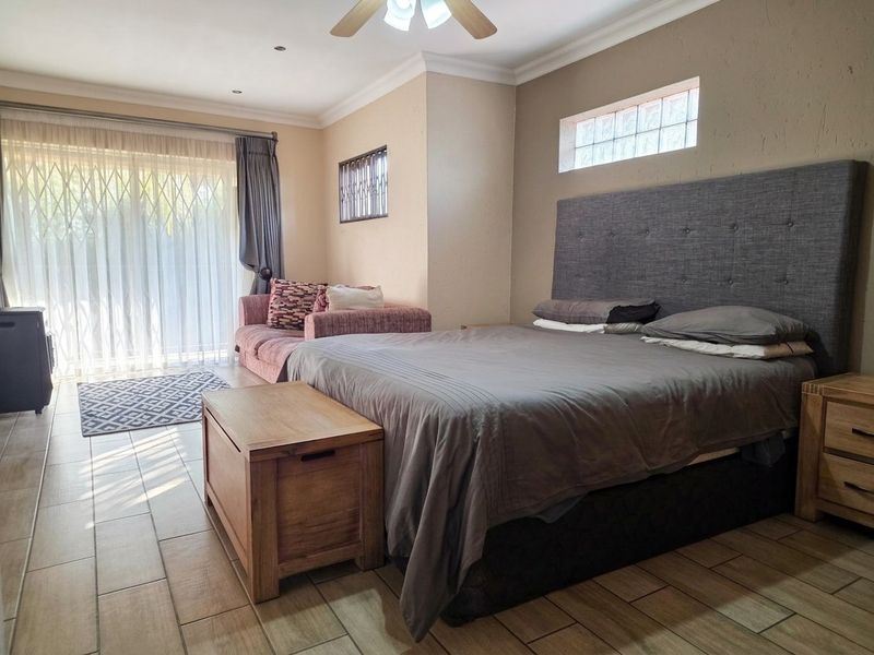 Spacious bedroom featuring tiled flooring, a ceiling fan, and a sliding door with security gate providing access to the exterior.