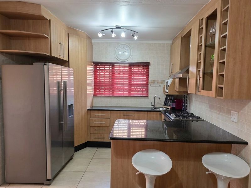 A functional kitchen featuring light wood cabinetry, dark granite countertops, a gas hob, extractor fan, and tiled flooring.