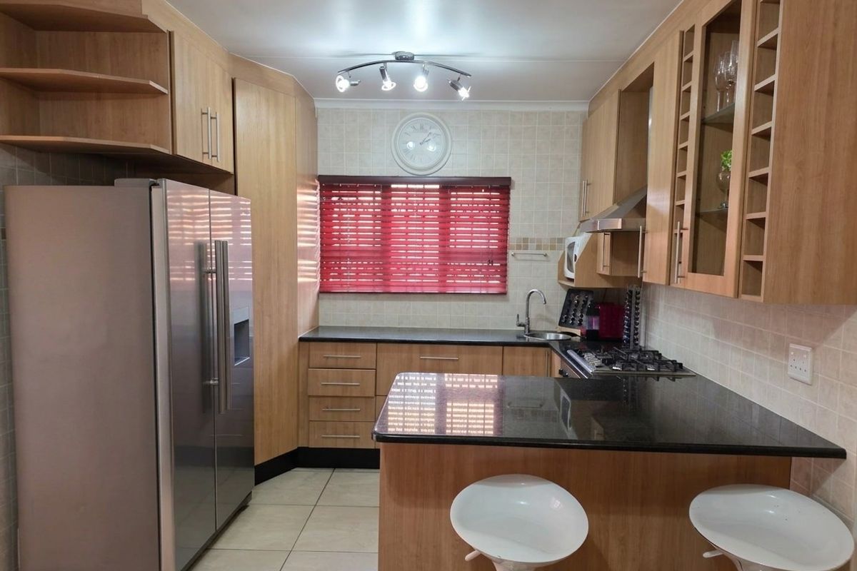 A functional kitchen featuring light wood cabinetry, dark granite countertops, a gas hob, extractor fan, and tiled flooring.