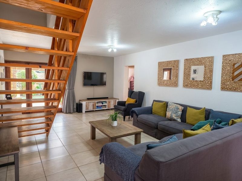 Spacious living room featuring tiled flooring and a prominent wooden staircase leading to the upper level, with direct access to the outdoor area.