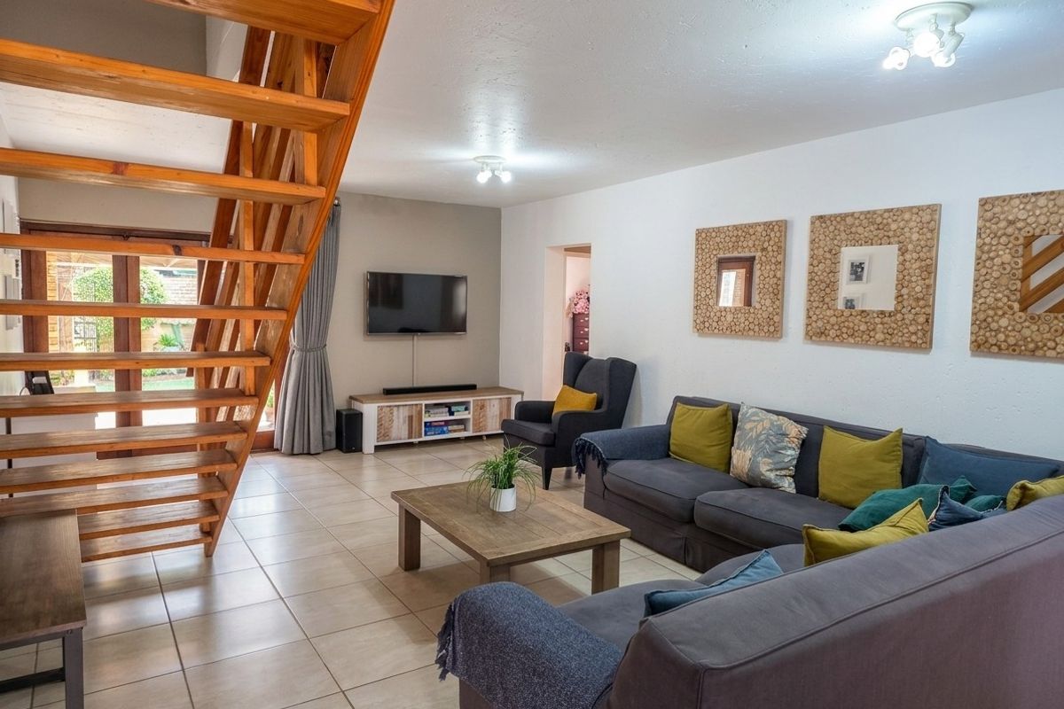 Spacious living room featuring tiled flooring and a prominent wooden staircase leading to the upper level, with direct access to the outdoor area.