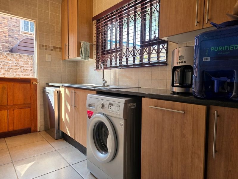 A functional kitchen featuring wood-look cabinetry, dark countertops, tiled splashbacks, and integrated space for laundry appliances with direct access to the exterior.