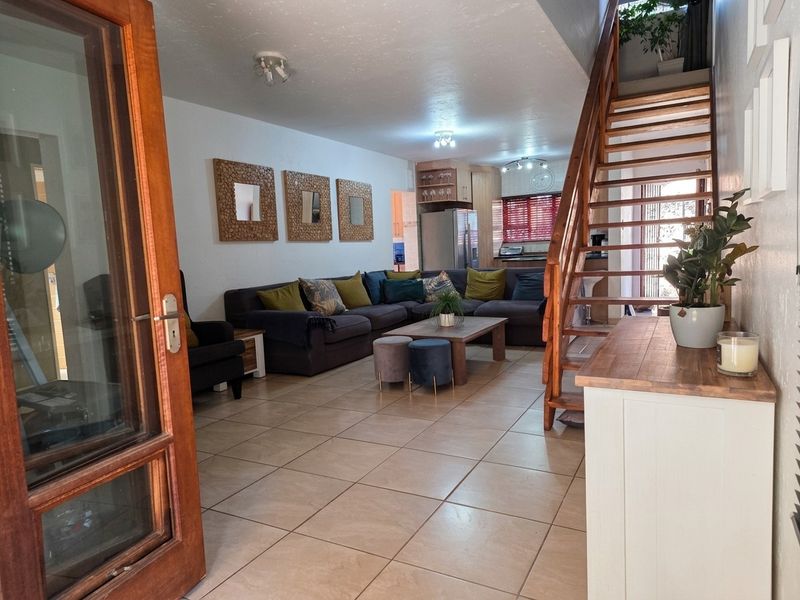 Open plan living area featuring tiled flooring, a wooden staircase, and a view through to the kitchen area.