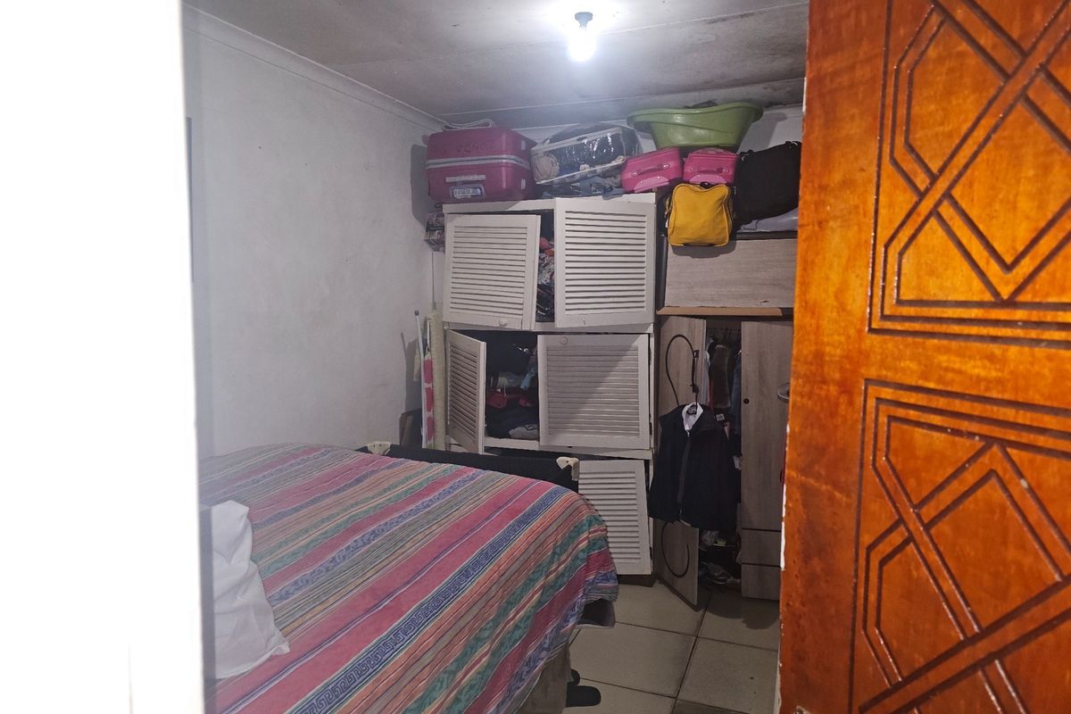 A small bedroom featuring tiled flooring and coved ceilings, currently showing signs of wear including ceiling staining and paint deterioration.
