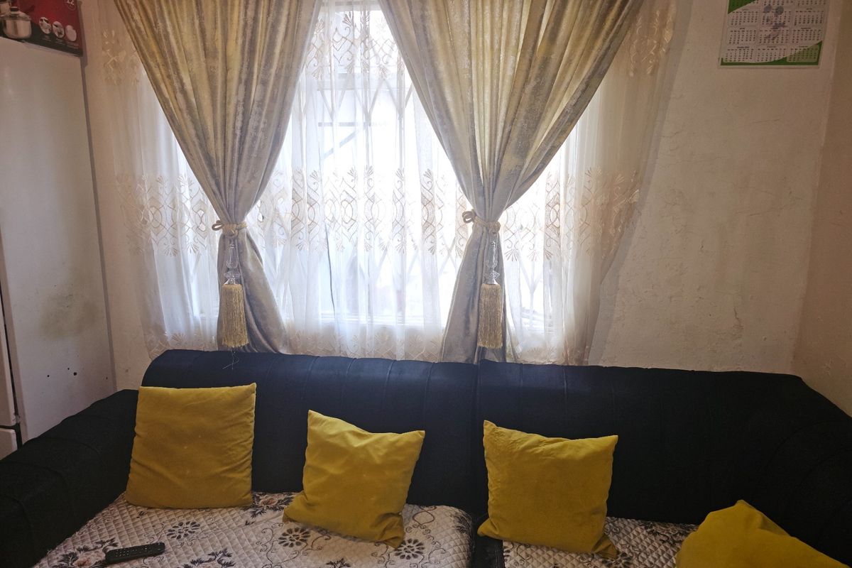 A living room area featuring a window with security gate and visible wall surface wear, requiring cosmetic attention.