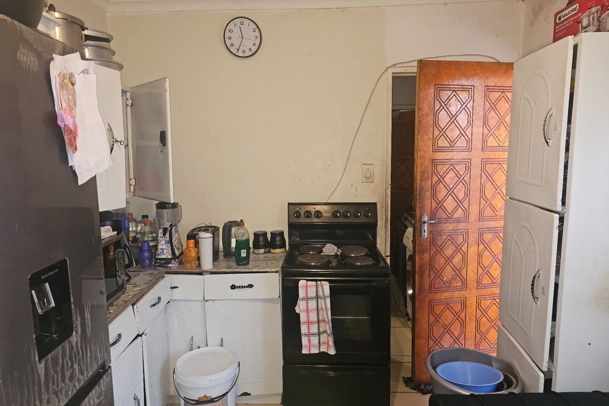 A functional kitchen featuring a freestanding stove, built-in cabinetry, and tiled flooring, currently requiring cosmetic updates and improved organization.