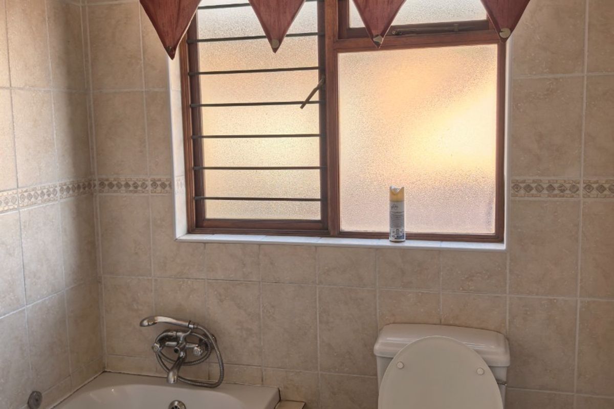 A functional bathroom featuring a built-in bathtub, a standard toilet, and tiled walls with a window providing natural light.
