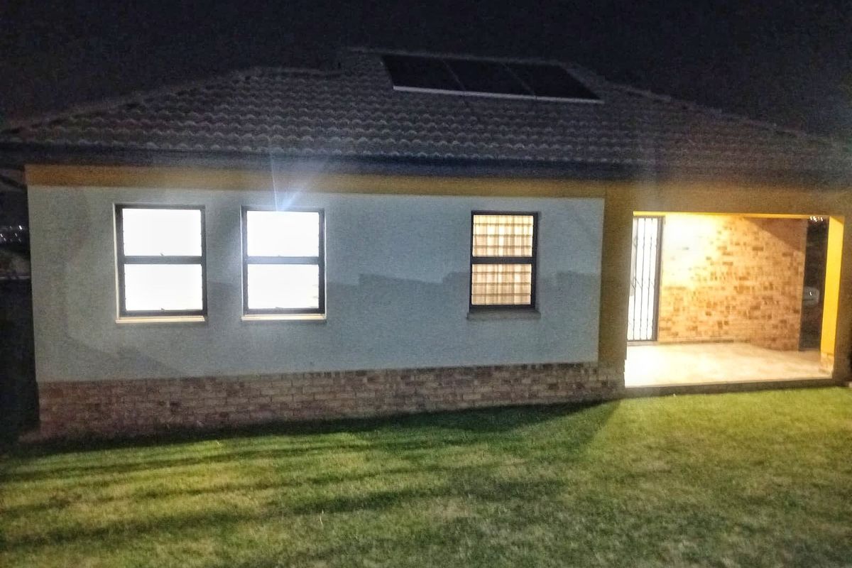 Night view of the rear exterior featuring a covered patio, brick facade detailing, and roof-mounted solar panels.