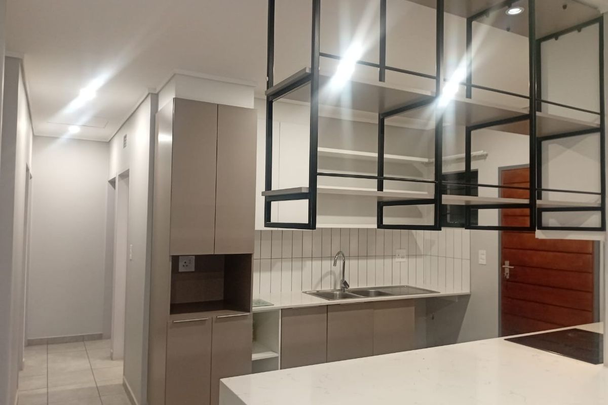 Modern kitchen featuring sleek cabinetry, stone countertops, a double sink, and a distinctive suspended black metal shelving unit above the breakfast bar.
