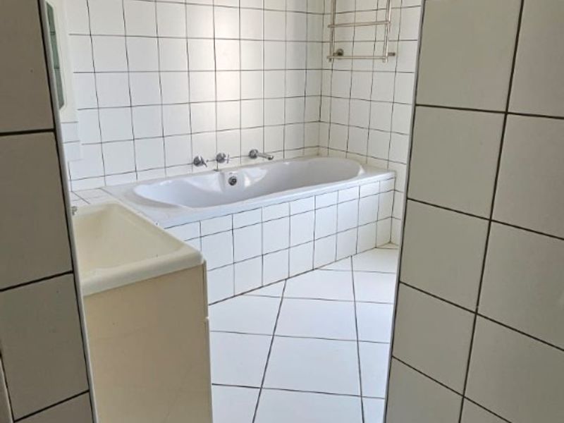 A functional bathroom featuring a built-in bathtub, tiled walls and flooring, and a wall-mounted towel rail.