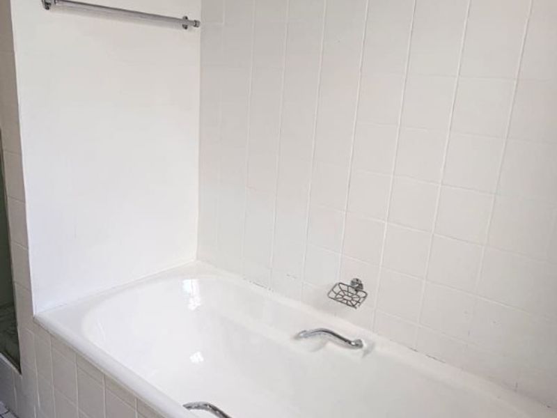 A functional bathroom featuring a built-in bathtub with white wall tiling and floor tiles.