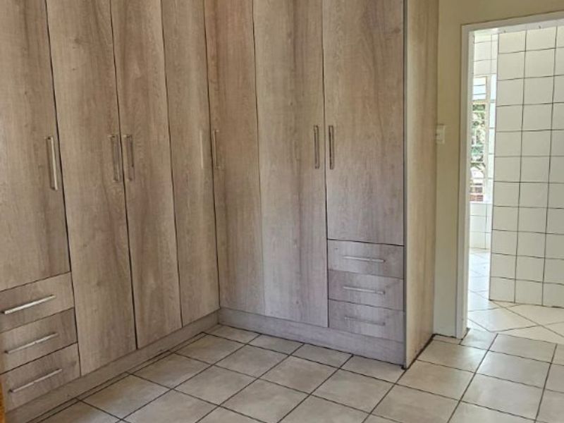 A bedroom featuring extensive floor-to-ceiling built-in wooden cabinetry with integrated drawers and tiled flooring, leading into an adjacent tiled bathroom.