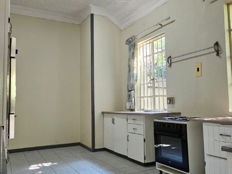 A dated kitchen featuring tiled flooring, basic cabinetry, a freestanding oven, and a textured ceiling with fluorescent lighting.