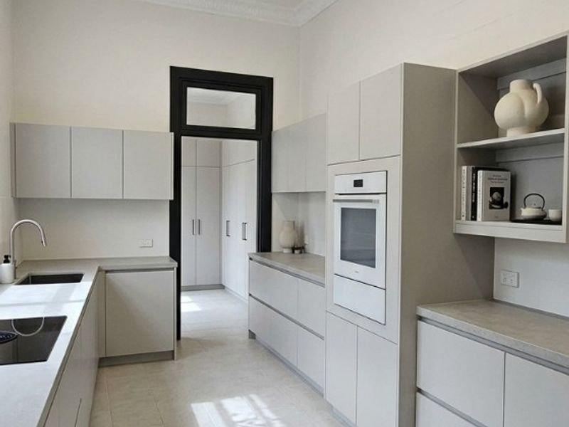 Modern galley-style kitchen featuring sleek cabinetry, integrated oven, stone-look countertops, tiled flooring, and a decorative pressed metal ceiling.