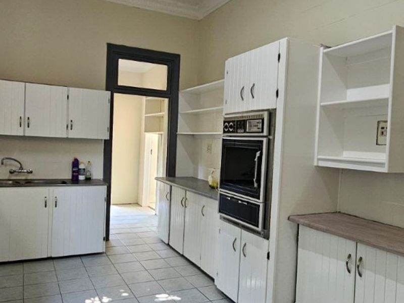 A dated kitchen featuring white cabinetry, built-in oven, tiled flooring, and a textured ceiling, offering significant potential for modernization and renovation.