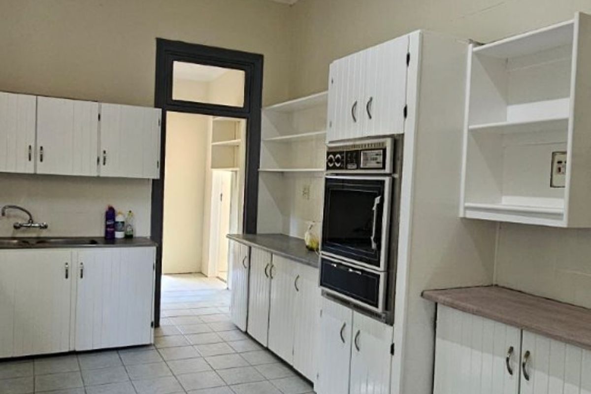 A dated kitchen featuring white cabinetry, built-in oven, tiled flooring, and a textured ceiling, offering significant potential for modernization and renovation.