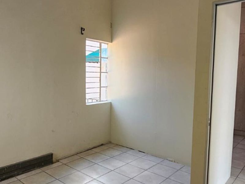 An empty, neutrally painted room featuring tiled flooring, a small window with security bars, and recessed ceiling lighting.