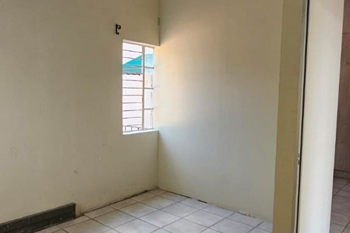 An empty, neutrally painted room featuring tiled flooring, a small window with security bars, and recessed ceiling lighting.