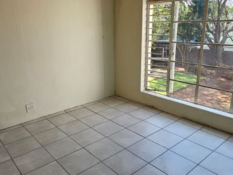 An empty bedroom featuring neutral tiled flooring, large window with security bars, and plain walls, offering a blank canvas for interior design.