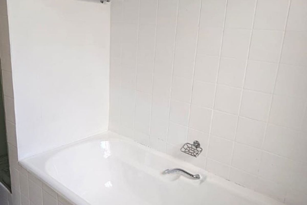A functional bathroom featuring a built-in bathtub with white wall tiling and floor tiles.