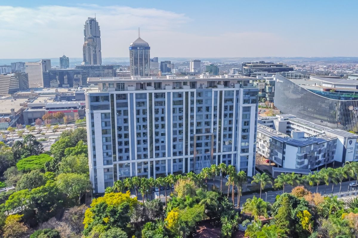 Aerial view of a modern high-rise penthouse building situated in a well-developed urban area with surrounding greenery and city skyline.