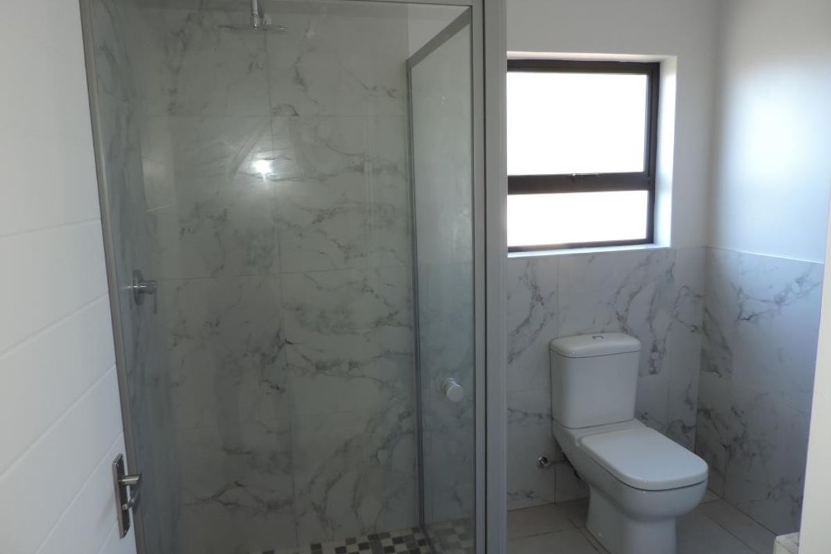 Modern bathroom featuring a glass-enclosed shower with marble-look wall tiles, mosaic floor tiling, and a white ceramic toilet.