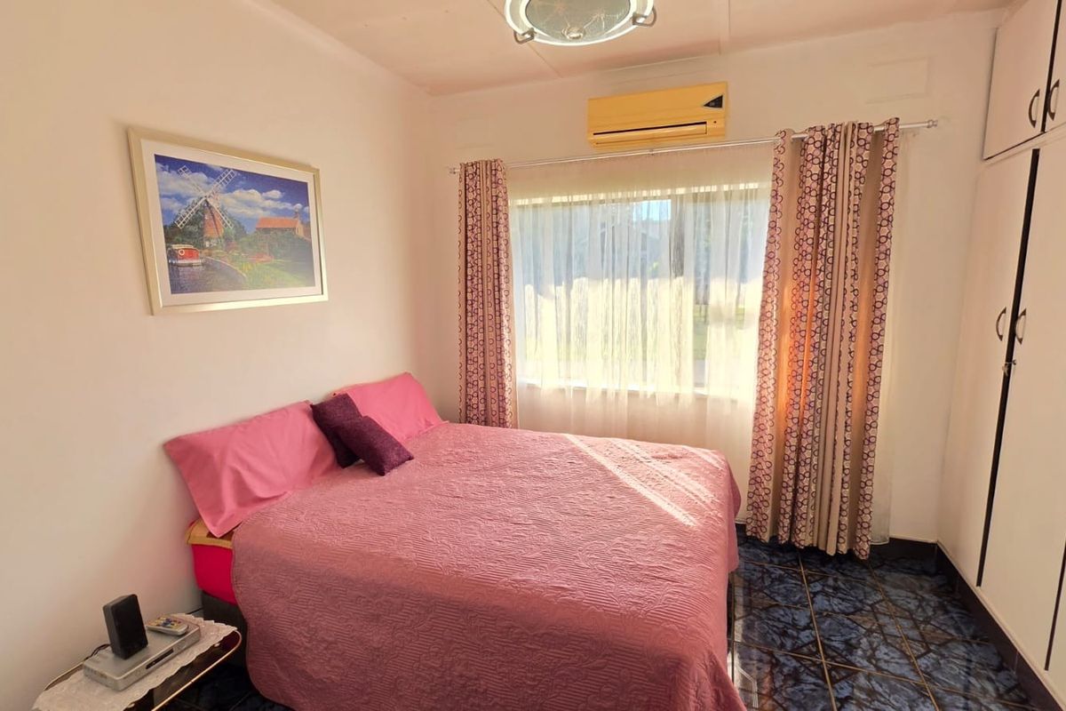 A bedroom featuring built-in cupboards, a wall-mounted air conditioning unit, and tiled flooring.