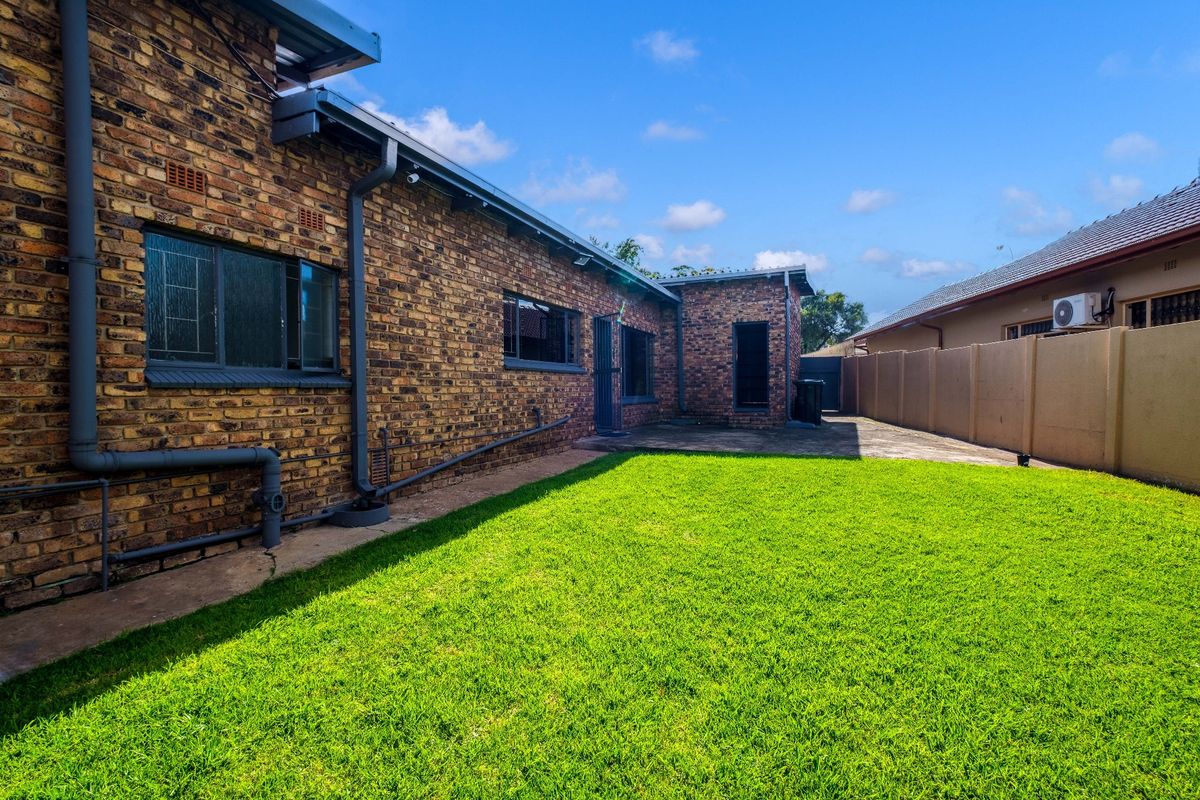 A view of the rear exterior of the house, featuring face-brick walls, a paved patio area, and a well-maintained lawn.