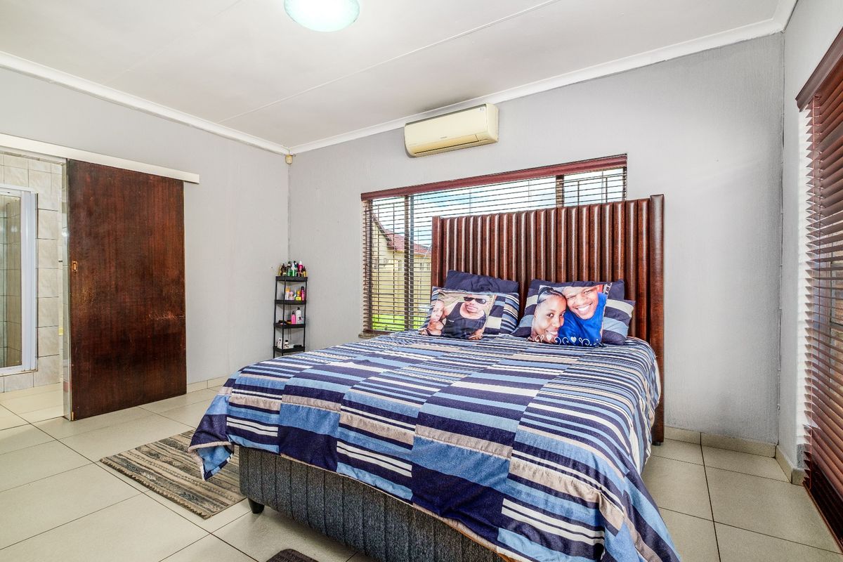 A bedroom featuring tiled flooring, a wall-mounted air conditioning unit, and an en-suite bathroom access via a sliding wooden door.
