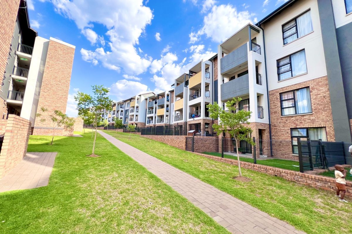 A view of the apartment complex exterior featuring brick facades, private balconies, and a well-maintained landscaped garden with a paved walkway.