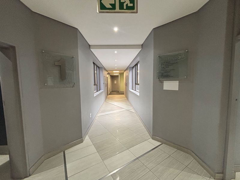A clean, well-lit office building hallway featuring tiled floors, recessed lighting, and professional glass directory signage for first-floor tenants.