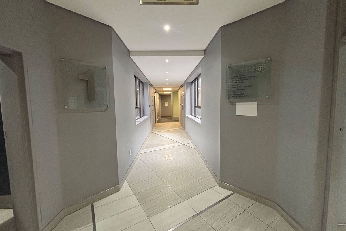 A clean, well-lit office building hallway featuring tiled floors, recessed lighting, and professional glass directory signage for first-floor tenants.