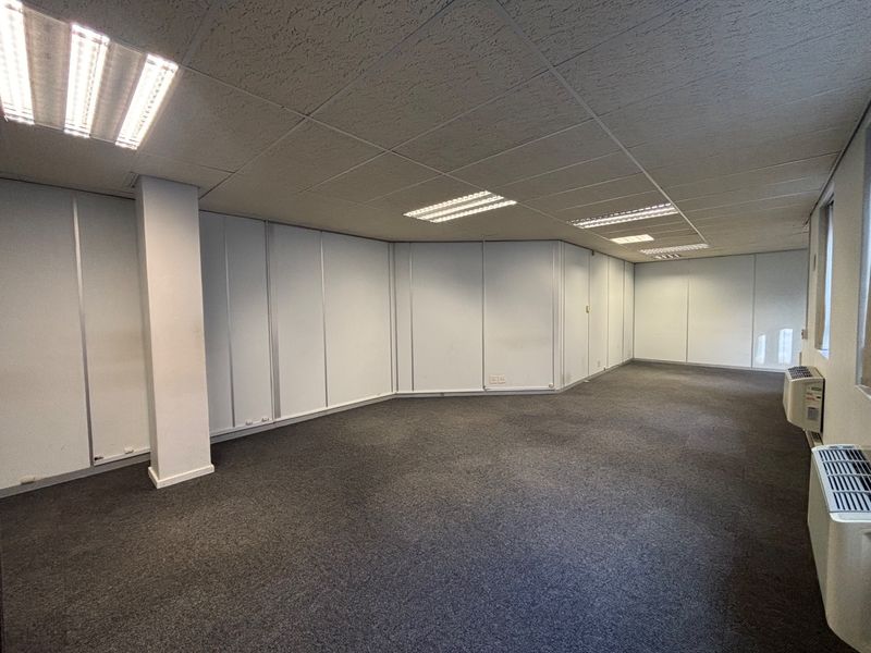 A spacious, empty office area featuring a suspended ceiling with recessed lighting, carpeted flooring, and integrated HVAC units.