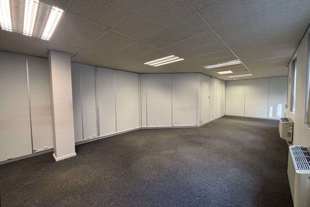 A spacious, empty office area featuring a suspended ceiling with recessed lighting, carpeted flooring, and integrated HVAC units.