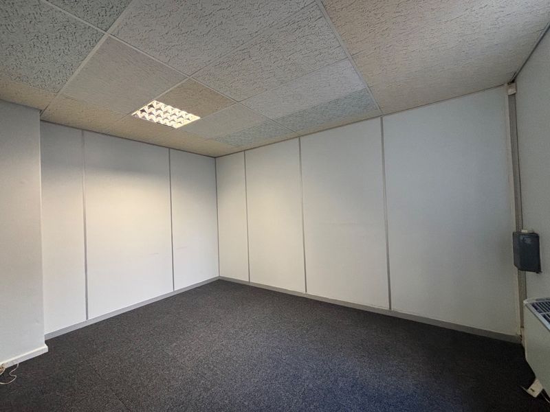 A vacant office space featuring neutral partition walls, carpeted flooring, and a suspended ceiling with integrated recessed lighting.