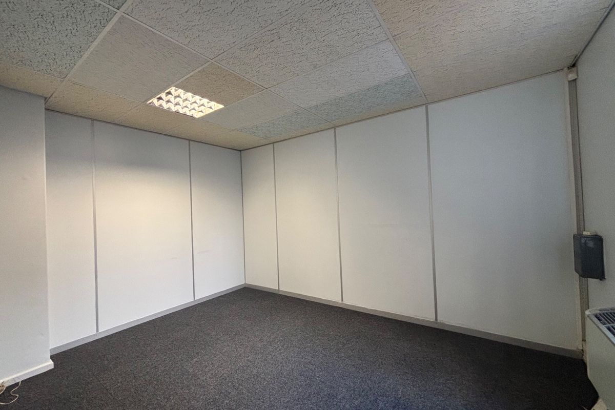 A vacant office space featuring neutral partition walls, carpeted flooring, and a suspended ceiling with integrated recessed lighting.