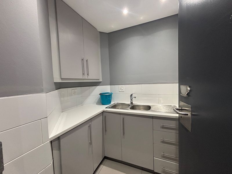 A compact, modern scullery area featuring grey built-in cabinetry, a stainless steel double sink, and a clean tiled backsplash.