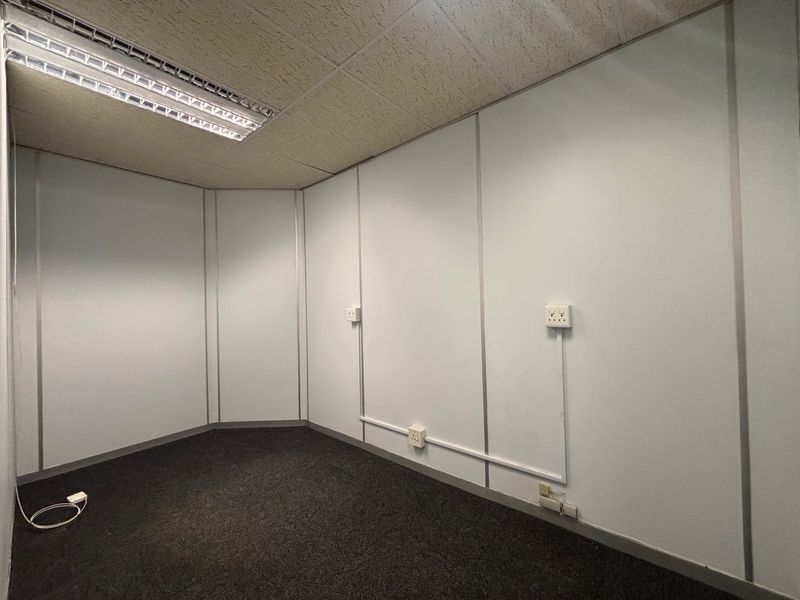 A vacant office space featuring modular partition walls, carpet flooring, and a suspended ceiling with recessed lighting, suitable for a professional workspace.
