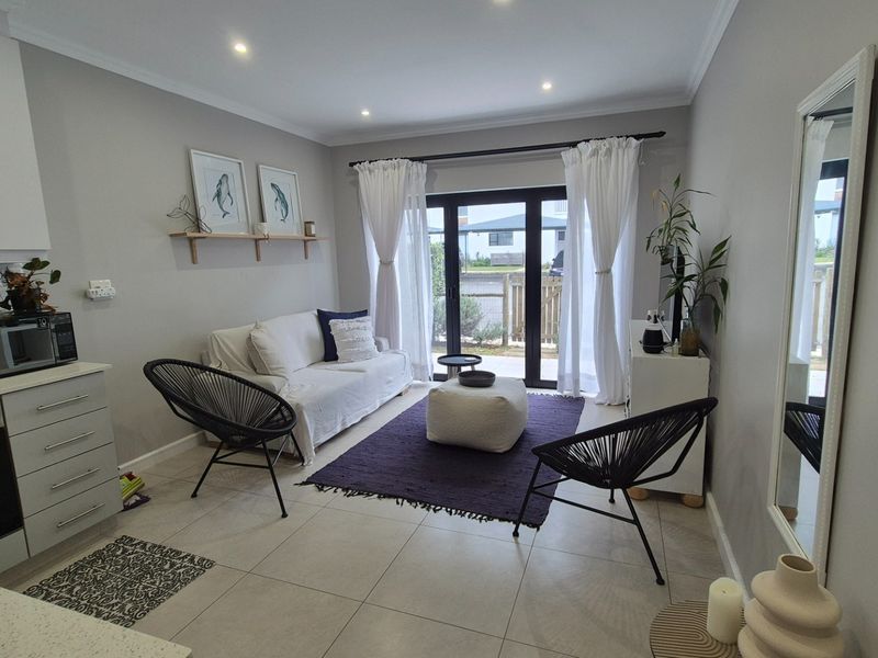 Modern open-plan living area featuring a compact kitchen with built-in appliances, tiled flooring, and large sliding glass doors leading to the exterior.